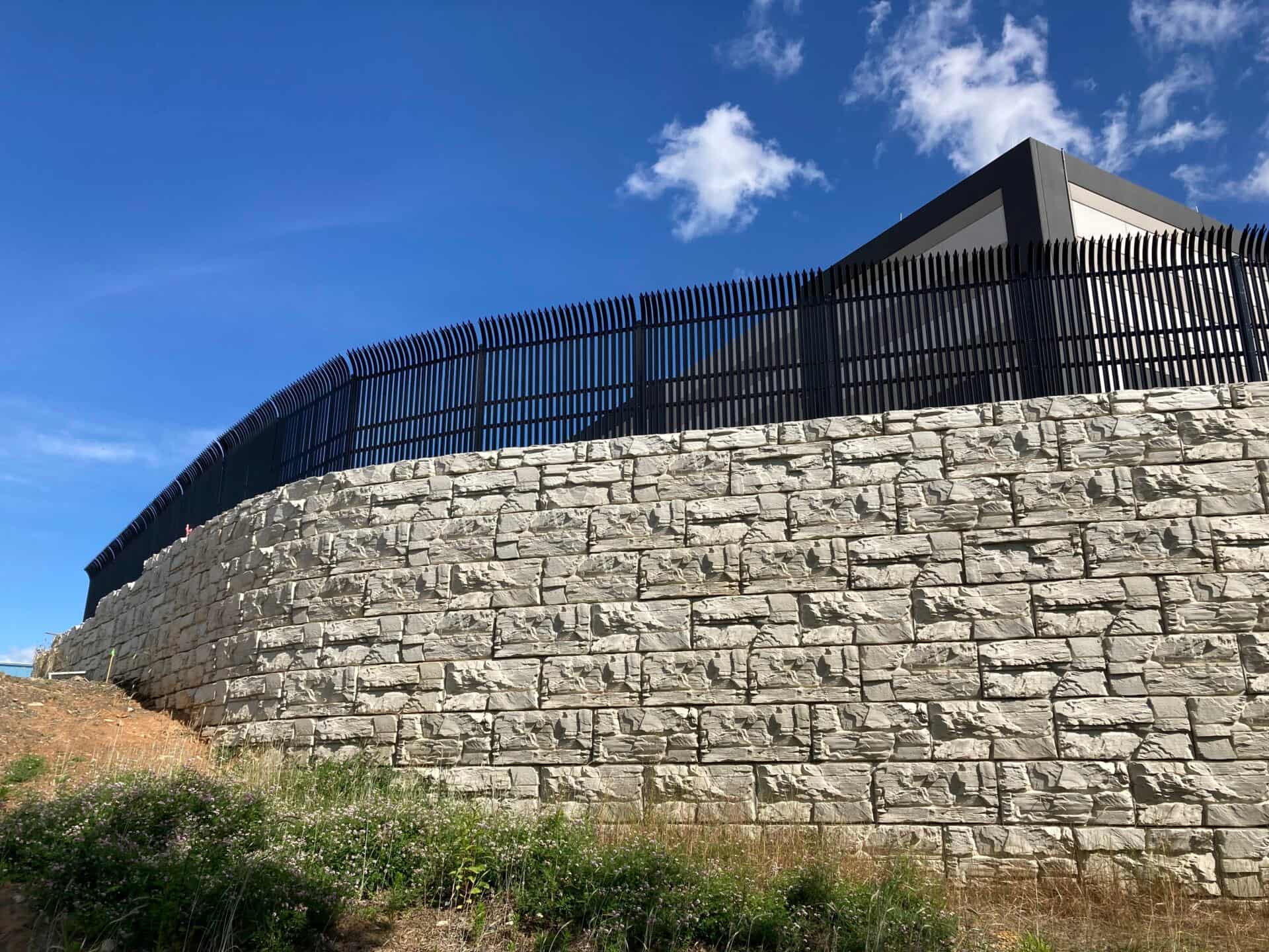 Tall engineered commercial retaining wall with safety fencing built by PacWest